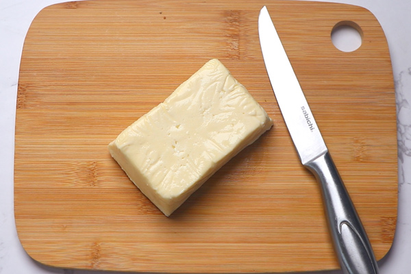 a cube of paneer on a chopping wooden board