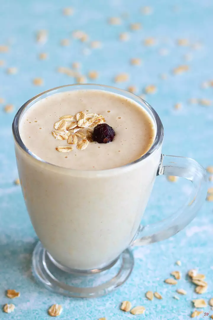 oats smoothie in a glass cup topped with rolled oats and dried cranberry