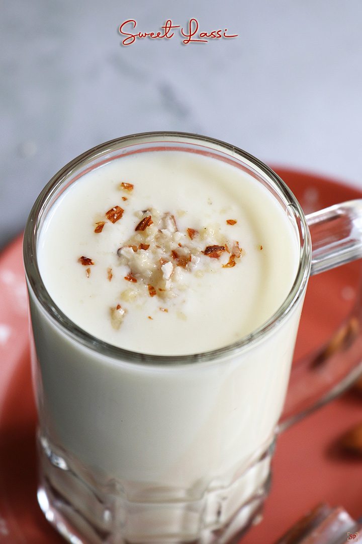 a close up shot of lassi served in a tall glass with crushed almonds as topping and a base plate