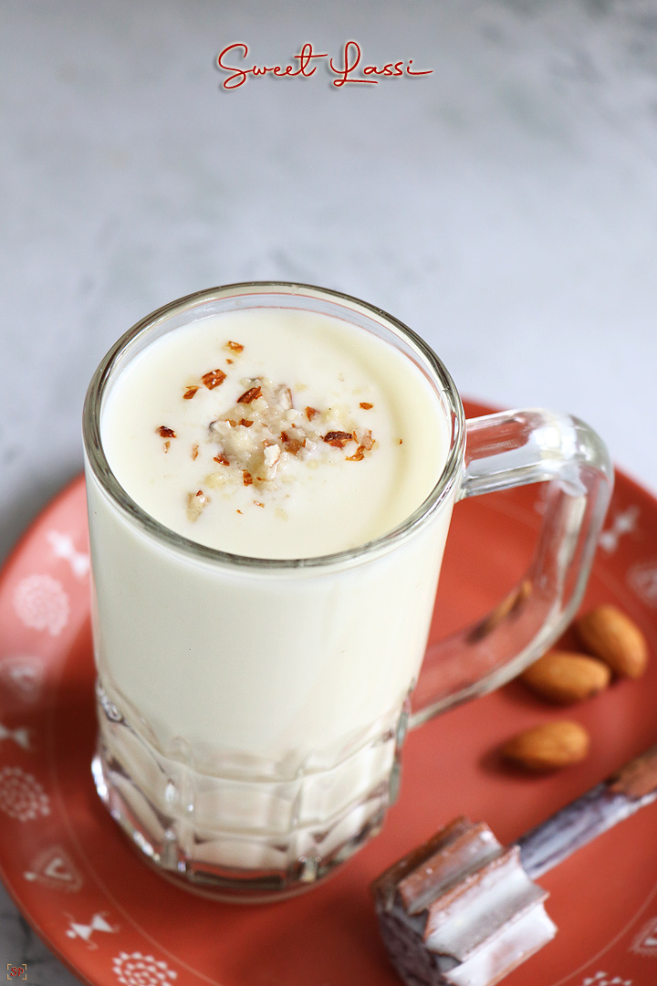 sweet lassi served in a tall glass with crushed nuts as topping