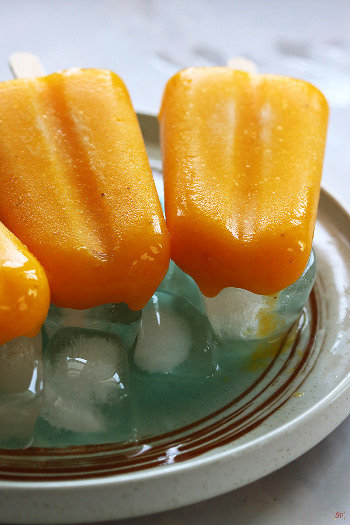 mango popsicles placed on a plate with ice cubes