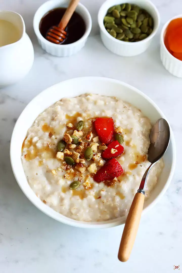 oatmeal porridge served in a white bowl with nuts and fruits topping