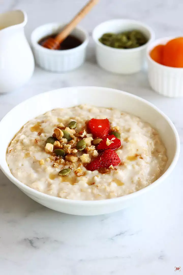 oatmeal porridge served in a white bowl with nuts and fruits topping