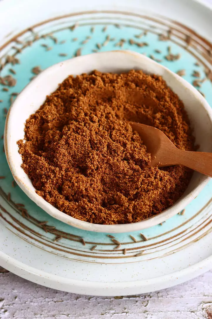 cumin powder in a small beige color bowl with a wooden spoon