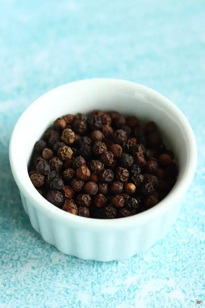 whole black pepper corns placed in a small white ramekin