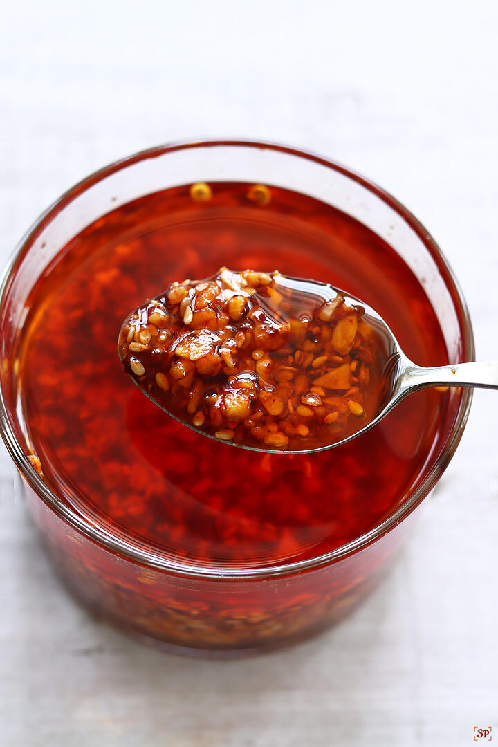 chilli oil in a glass jar with a spoon showing chilli oil and chilli crisp